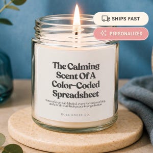 May include: A clear glass jar candle with a lit wick and a white label featuring black text that reads The Calming Scent Of A Color-Coded Spreadsheet, Notes of every tab labelled, every formula working, and a brain that finds peace in organisation.