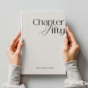 May include: A white book with the words "Chapter Fifty" in elegant black script. The author's name, "MIA WILLIAMS," is printed below. The book is held by two hands with manicured nails.