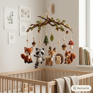 May include: A woodland-themed nursery mobile featuring a brown branch structure with green leaves and hanging crochet figures including a fox, raccoon, deer, hedgehog, squirrel, pine tree, mushrooms, and acorns suspended by light-colored twine.