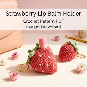 May include: Two strawberry-shaped crochet lip balm holders with green leaves and gold-toned keyrings. One holder contains a pink lip balm tube. The text "Strawberry Lip Balm Holder Crochet Pattern PDF Instant Download" is visible above.