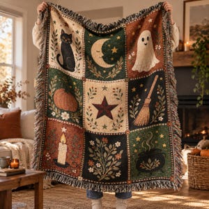 May include: A woven throw blanket featuring a grid of nine squares with Halloween-themed illustrations including a black cat, a crescent moon, a ghost, a pumpkin, a star, a broom, a lit candle, floral foliage, and a steaming cauldron.