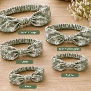 May include: Five sage green headbands with a white floral pattern, each featuring a knotted bow detail and an elasticised back. The headbands are labelled with text indicating sizes: Adult / Large, Teen / Small Adult, Child, Toddler, and Baby.