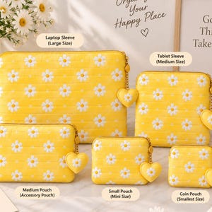 May include: A collection of five yellow quilted pouches and sleeves featuring a white daisy pattern. Each item includes a heart-shaped zipper pull. The set includes a laptop sleeve, tablet sleeve, medium accessory pouch, small pouch, and coin pouch.