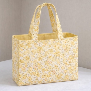 May include: A rectangular tote bag with a floral pattern in yellow and white. The bag has two handles and a solid yellow interior. The bag is approximately 30 cm wide, 25 cm tall, and 10 cm deep.