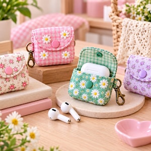 Puede incluir: Cuatro fundas de tela para auriculares con cierres a presión y clips metálicos. Una funda es rosa con margaritas blancas, una es crema con pequeñas flores rosas, una es verde con margaritas blancas y una es morada con pequeñas flores moradas.
