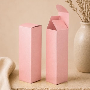 May include: Two tall, rectangular, light pink paper boxes. One box is fully closed with a flat top, while the other box is open at the top with its flaps partially extended upward. The boxes have a smooth, matte finish and a vertical orientation.