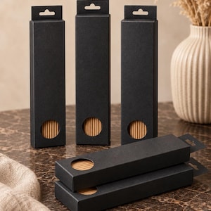 May include: Five tall, rectangular black cardboard boxes with a matte finish, each featuring a circular cutout near the bottom that reveals light brown, ribbed cylindrical contents inside. Three boxes stand upright, while two are stacked horizontally.
