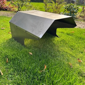 May include: A dark gray metal robotic lawn mower shelter featuring a slanted roof design and open sides. The structure is constructed from bent sheet metal panels secured with visible rivets along the edges, providing a protective cover.