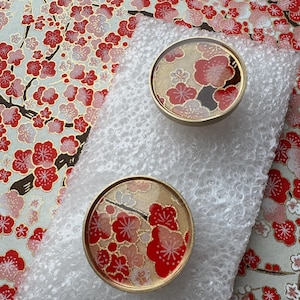 Peut inclure: Deux boutons de porte ronds décoratifs avec un bord doré et un motif floral avec des fleurs rouges et roses. Les boutons sont sur du papier bulle, avec un fond à motifs floraux rouges, roses et dorés.