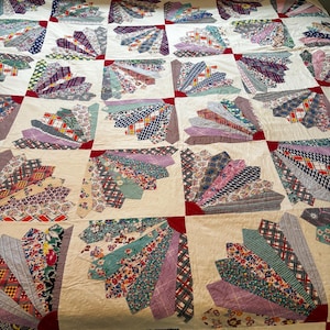 Puede incluir: Un edredón hecho a mano con un diseño de abanico. El edredón presenta un fondo color crema con diseños en forma de abanico en varios colores y patrones, incluyendo estampados florales, a cuadros y geométricos. Los acentos de esquina rojos añaden contraste.