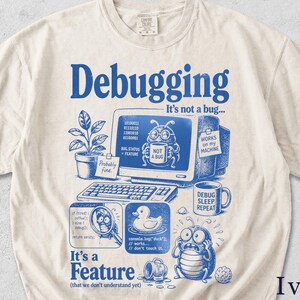 Könnte beinhalten: Ein elfenbeinfarbenes T-Shirt mit blauem Grafikdruck und dem Text Debugging It's not a bug... It's a Feature (that we don't understand yet). Das Design zeigt einen Computer, eine Topfpflanze, eine Quietscheente und eine Käferfigur mit Tasse.