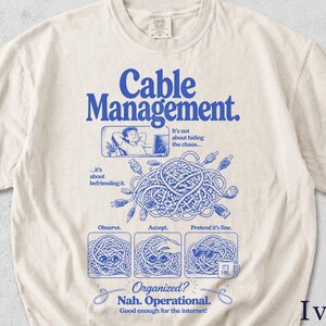 Könnte beinhalten: Elfenbeinfarbenes T-Shirt mit einem blauen Aufdruck mit der Aufschrift "Cable Management". Die Grafik zeigt eine Person, die sich mit einem Laptop entspannt, ein Kabelsalat und die Sätze "Observe", "Accept" und "Pretend it's fine". Der Text "Organized? Nah. Operational" ist ebenfalls enthalten.