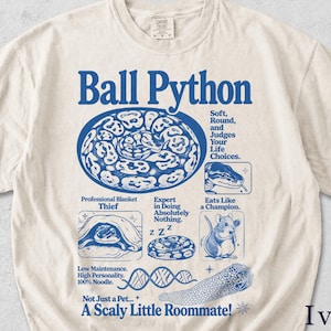 Könnte beinhalten: Elfenbeinfarbenes T-Shirt mit blauem Grafikdesign, das eine Kugelpython und Text zeigt. Der Text enthält "Ball Python" und humorvolle Beschreibungen wie "Professional Blanket Thief" und "A Scaly Little Roommate!"
