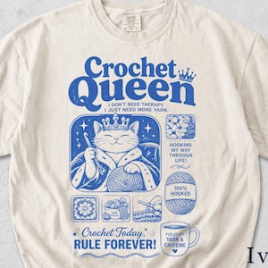 Könnte beinhalten: Elfenbeinfarbenes T-Shirt mit blauem Aufdruck. Das Design zeigt eine Katze mit Krone, die einen Häkelhaken und Wolle hält. Der Text enthält "Crochet Queen", "I don't need therapy, I just need more yarn" und "Crochet Today, Rule Forever!"