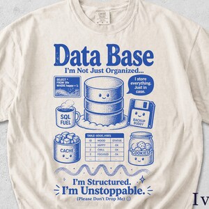 Op de afbeelding: Ivoor t-shirt met een blauw grafisch ontwerp. Het ontwerp toont de woorden "Data Base" en verschillende computergerelateerde illustraties, waaronder een database, een diskette en een pot koekjes. Tekst bevat "I'm Not Just Organized..." en "I'm Structured. I'm Unstoppable."