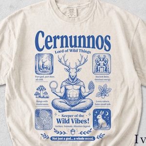 May include: Ivory-colored t-shirt featuring a blue graphic of Cernunnos, the Lord of Wild Things. The design includes a deer-headed figure, text, and illustrations of nature elements. The text reads "Keeper of the Wild Vibes!" and "Not just a god... a whole mood."