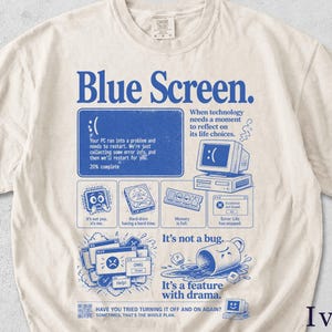 May include: Ivory-colored t-shirt with a blue graphic design. The design features the words "Blue Screen" and a computer error message, along with illustrations of computer components and the text "It's not a bug. It's a feature with drama."