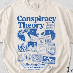 May include: An ivory short-sleeve t-shirt featuring a blue graphic print with the text Conspiracy Theory, Question everything! Especially this shirt, Hidden Truths, Today's Agenda, Trust No One Except Dogs, and Collecting Clues Since Forever! Not crazy. Just early.