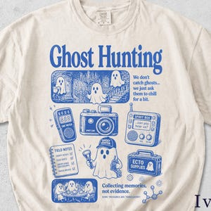 May include: An ivory t-shirt featuring a blue graphic print with the text Ghost Hunting. The design includes illustrations of ghosts, an EMF meter, a spirit camera, a spirit box, field notes, and a supply case with the text Ecto Supplies.