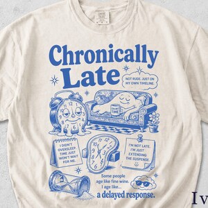Op de afbeelding: Ivoorkleurig T-shirt met een blauwe opdruk met de tekst "Chronisch te laat". Het ontwerp bevat een smeltende klok, een persoon op een bank en andere illustraties over tijd. Het shirt heeft een relaxte pasvorm.