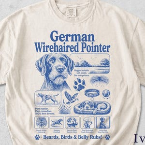 Könnte beinhalten: Ein elfenbeinfarbenes T-Shirt mit einem blauen Grafikdruck eines Deutsch Drahthaars. Das Design zeigt das Porträt des Hundes, eine Landschaft, einen Pfotenabdruck, ein Halsband, einen Ball und Text wie "Part hunter. Part comedian. 100% Best Friend."