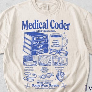 Könnte beinhalten: Ein elfenbeinfarbenes T-Shirt mit kurzen Ärmeln und blauen grafischen Illustrationen sowie Text. Das Design zeigt einen Stapel medizinischer Bücher, eine Kaffeetasse, eine Brille, ein Stethoskop, einen DNA-Strang und ein Herz, mit dem Text Medical Coder und Not All Heroes Wear Capes. Some Wear Scrubs.
