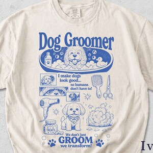 May include: An ivory t-shirt featuring a blue graphic print with the text Dog Groomer, I make dogs look good... so humans don't have to!, and We don't just GROOM we transform!. The design includes illustrations of dogs, a tub, shampoo, and tools.