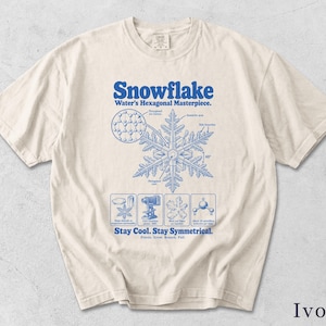 Könnte beinhalten: Ein elfenbeinfarbenes T-Shirt mit einem blauen Grafikdruck eines Schneeflockendiagramms. Der Text lautet Snowflake, Water's Hexagonal Masterpiece, Stay Cool. Stay Symmetrical. Freeze. Grow. Branch. Fall. Es enthält wissenschaftliche Darstellungen von Eiskristallen.