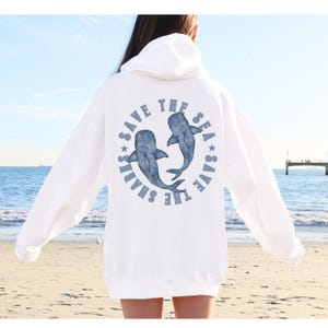 Könnte beinhalten: Weißer Hoodie mit einem blauen Aufdruck auf der Rückseite, der "Save the Sharks Save the Sea" lautet, mit zwei blauen Walhaien in der Mitte des Kreises.
