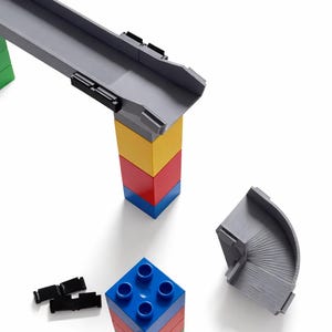 Könnte beinhalten: Ein farbenfrohes Spielzeug-Baustein-Set mit einer grauen Bahn und gebogenen Teilen. Die Blöcke sind rot, gelb, blau und grün. Die Bahn wird von einem Turm aus Blöcken getragen. Das Set befindet sich auf weißem Hintergrund.