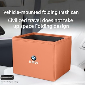 以下が含まれることがあります： BMWのロゴが入った、オレンジ色の長方形の車載用折りたたみ式ゴミ箱。 ゴミ箱の内部は黒色で、省スペースで収納できるように折りたためるように設計されています。 画像のテキスト: 車載用折りたたみ式ゴミ箱、文明的な旅行は場所を取らない、折りたたみ設計。