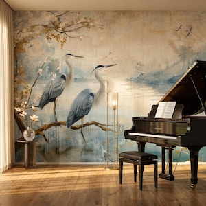 May include: A black grand piano with a matching bench sits on a wooden floor in front of a large wall mural. The mural features two grey herons perched on a branch, surrounded by soft blue and gold watercolour-style landscape imagery.