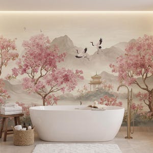 May include: A white freestanding bathtub sits in front of a wall mural featuring pink cherry blossom trees, two flying cranes, and a pagoda nestled among mountains. A brass floor-mounted faucet stands beside the tub, with a wooden stool and basket nearby.