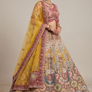 May include: A lehenga choli set featuring a magenta blouse with intricate embroidery and a voluminous skirt with a multi-colored geometric pattern, peacock motifs, and a sheer yellow dupatta with a wide, ornate magenta border and gold trim.