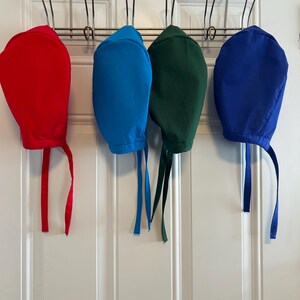 May include: Four surgical caps hanging on hooks. The caps are red, blue, green, and light blue.