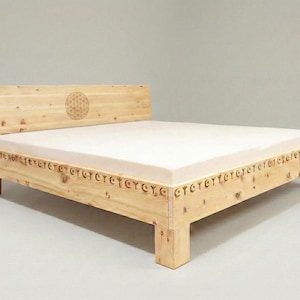 Könnte beinhalten: Ein hellfarbiger Holzbettenrahmen mit einem Kopfteil mit einem geschnitzten Blumendesign. Der Bettrahmen hat dekorative Schnitzereien an den Seiten und eine weiße Matratze. Das Bett ist aus Naturholz gefertigt.