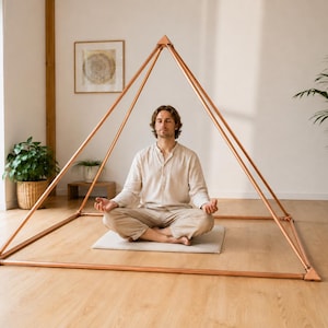 May include: A large, hollow, four-sided pyramid frame constructed from metallic copper-colored tubing. The structure features straight rods connected at the base corners and apex with triangular joints, creating a geometric open-frame design.