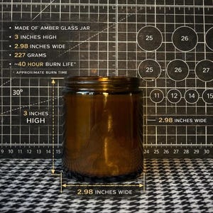 May include: An amber glass candle jar measuring 3 inches high and 2.98 inches wide. The jar weighs 227 grams and features an approximate 40-hour burn life. The text on the image specifies these dimensions and the burn time for the glass container.
