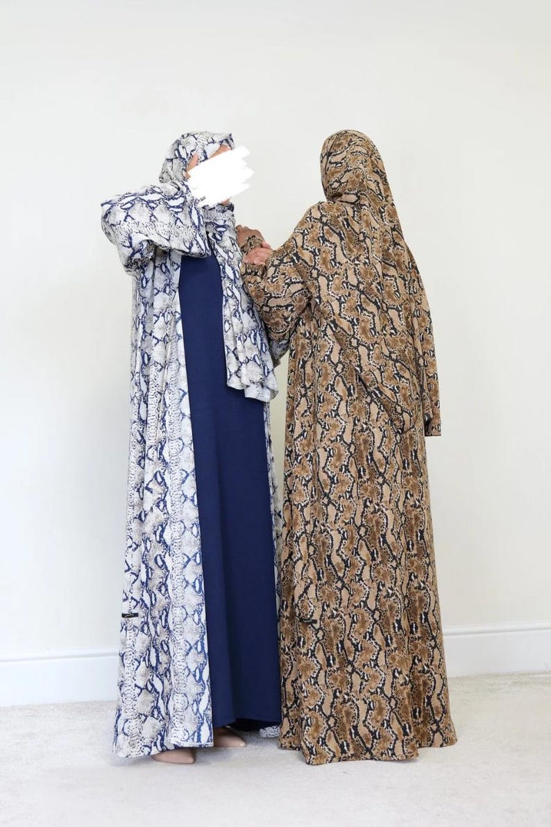 May include: Two full-length abayas. One is navy blue with a white and blue snakeskin print outer layer. The other is brown and tan snakeskin print. Both have matching head coverings. The abayas are worn by two people.
