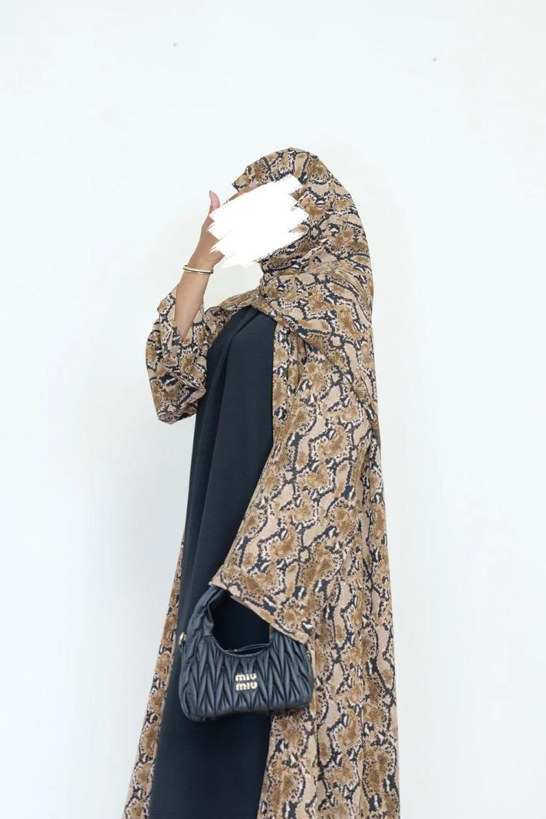 May include: A black dress is worn with a snakeskin-patterned outer garment. A small, black handbag with a quilted design is held. A gold bracelet completes the outfit.