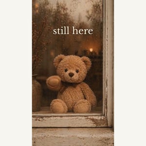 May include: A light brown plush teddy bear sits on a window ledge next to a vase with dried branches. The window glass is covered in raindrops and features the text still here in white lettering. The scene has a warm, muted color palette.