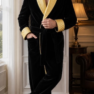 May include: A black velvet robe featuring a quilted gold shawl collar and matching quilted gold cuffs. The robe includes a tie belt at the waist and two front pockets. The fabric has a smooth, soft texture with a slight sheen, contrasting with the gold.