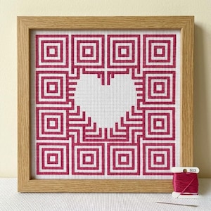 May include: Cross-stitch picture in a wooden frame. The design shows a white heart shape surrounded by a pattern of red squares and lines. A spool of red thread and a needle are visible in the lower right corner.