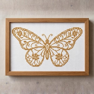 Pode incluir: Uma cruz bordada emoldurada de uma borboleta. A borboleta é amarelo-dourado com detalhes intrincados, contra um fundo branco. A moldura é de madeira castanha clara. Uma peça decorativa.