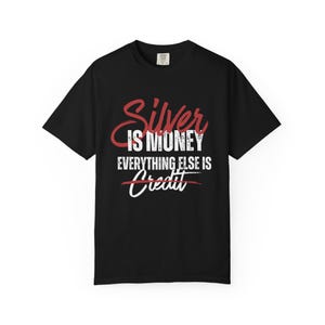 May include: Black t-shirt with the text "Silver is Money, Everything Else is Credit" in red and white. The word "Credit" is crossed out. The shirt has a crew neck and short sleeves.
