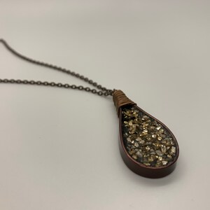 May include: A teardrop-shaped pendant necklace with a copper chain. The pendant is filled with gold glitter and encased in clear resin.