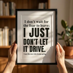 Pode incluir: Uma moldura preta contendo uma impressão com fundo branco e texto preto em negrito que diz: I don't wait for the fear to leave; I JUST DON'T LET IT DRIVE. Abaixo, um texto menor diz: I am the one who keeps going.
