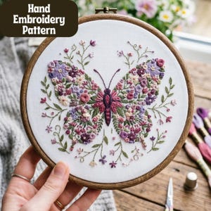 Puede incluir: Patrón de bordado a mano con diseño de mariposa. La mariposa está llena de bordados florales morados, rosas y blancos sobre tela blanca. El bordado está en un aro de madera, con el texto "Hand Embroidery Pattern" en la esquina superior izquierda.
