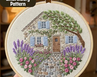 May include: Hand embroidery pattern of a stone cottage with blue shutters, a wooden door, and a cobblestone path. Lavender and pink roses frame the house. The text "Hand Embroidery Pattern" is in the upper left corner. The embroidery is set in a wooden hoop.