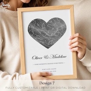 Puede incluir: Una impresión enmarcada con un mapa estelar en forma de corazón con constelaciones sobre un fondo gris oscuro. Debajo del corazón, el texto dice Oliver & Madeline, Some moments change everything, Portland, Maine, y August 18th 2026 en negro.